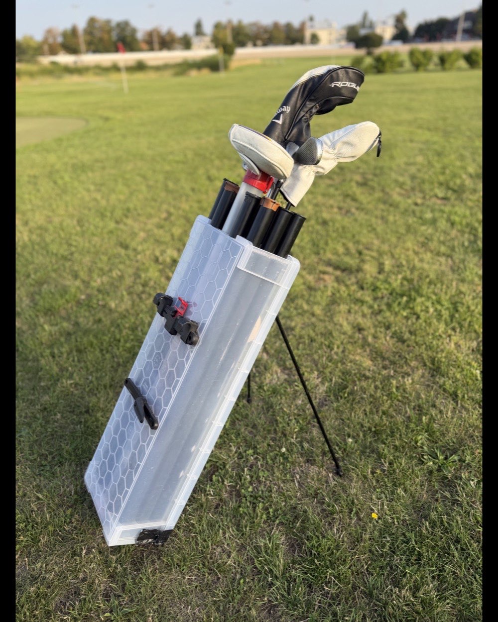 The prototype standing upright on the grass with irons and two headcovers visible, green and flag behind.