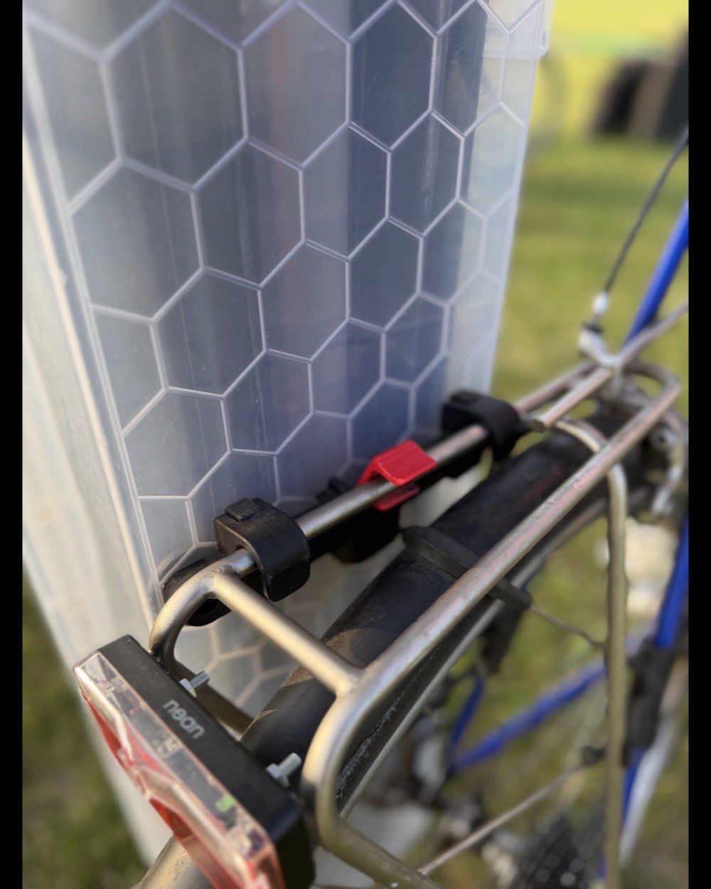 Close-up of the KlickFix hook and its red release lever clamped over the round tube of a bike's rear rack, the case wall beside it.