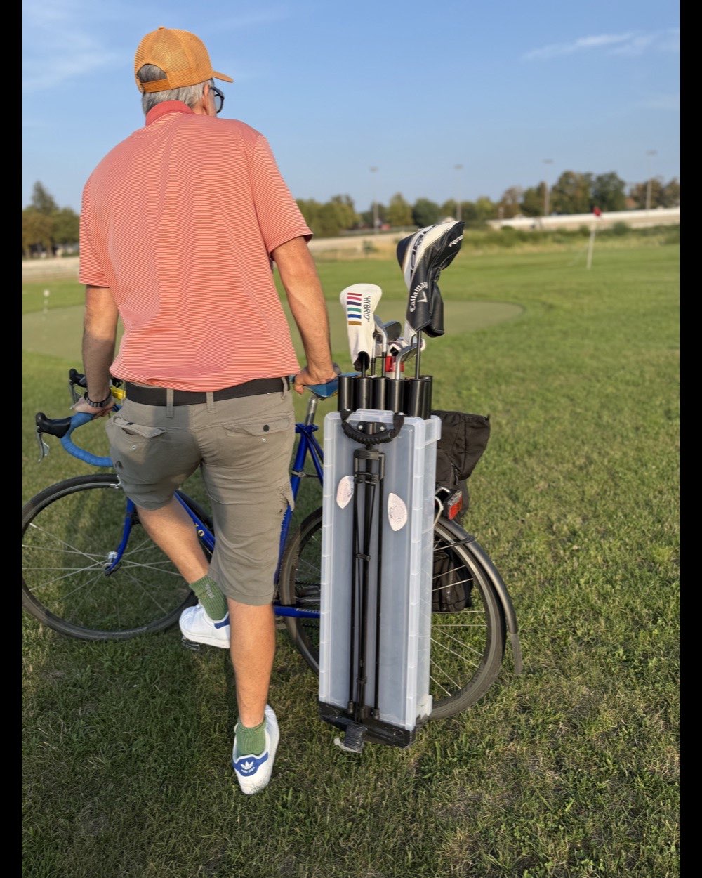 A golfer pushing the loaded bike across the grass, the case mounted on the rear rack beside a pannier.