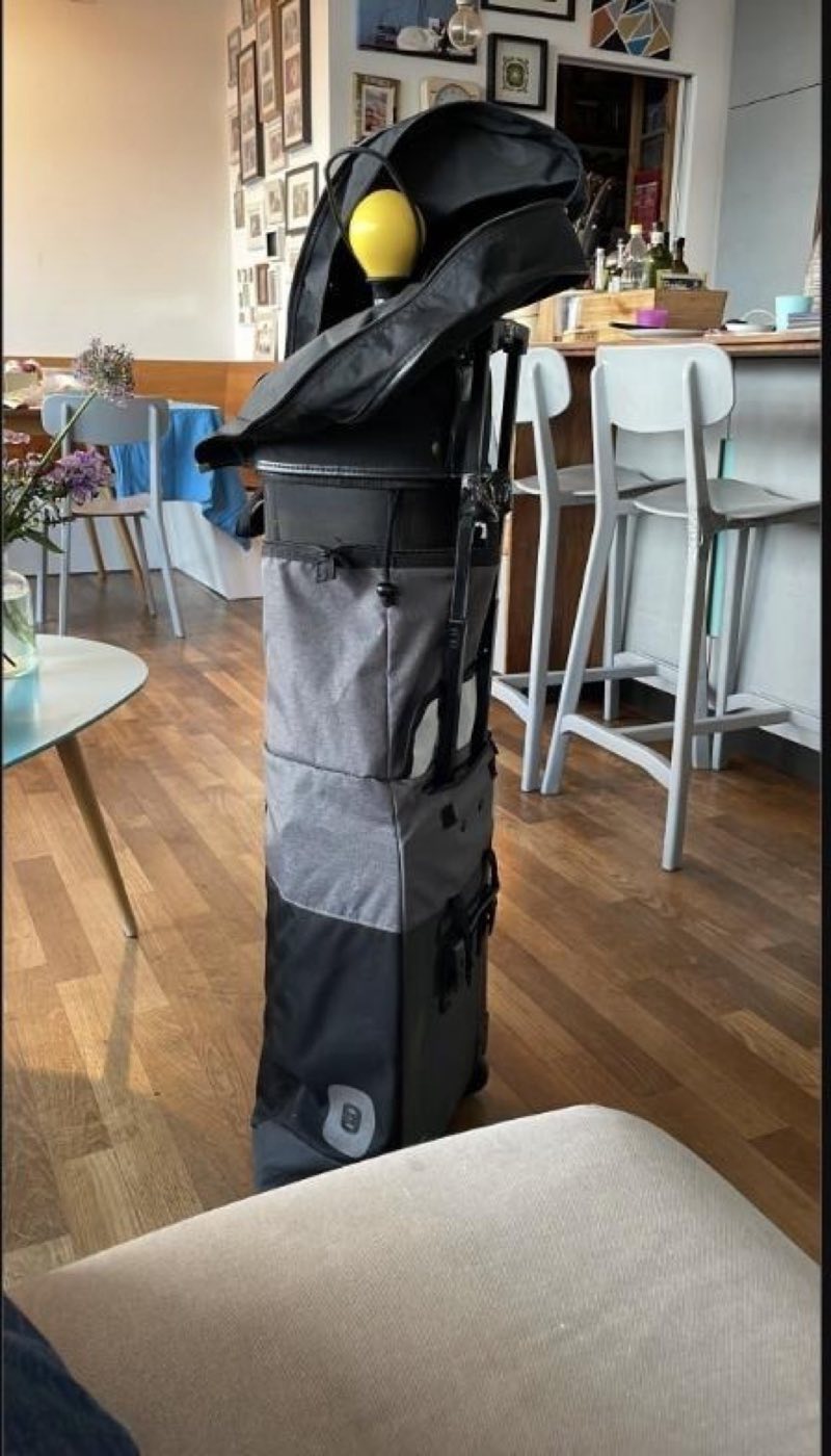 The v2 prototype standing on a wooden floor with clubs and a yellow driver headcover sticking out of the top.