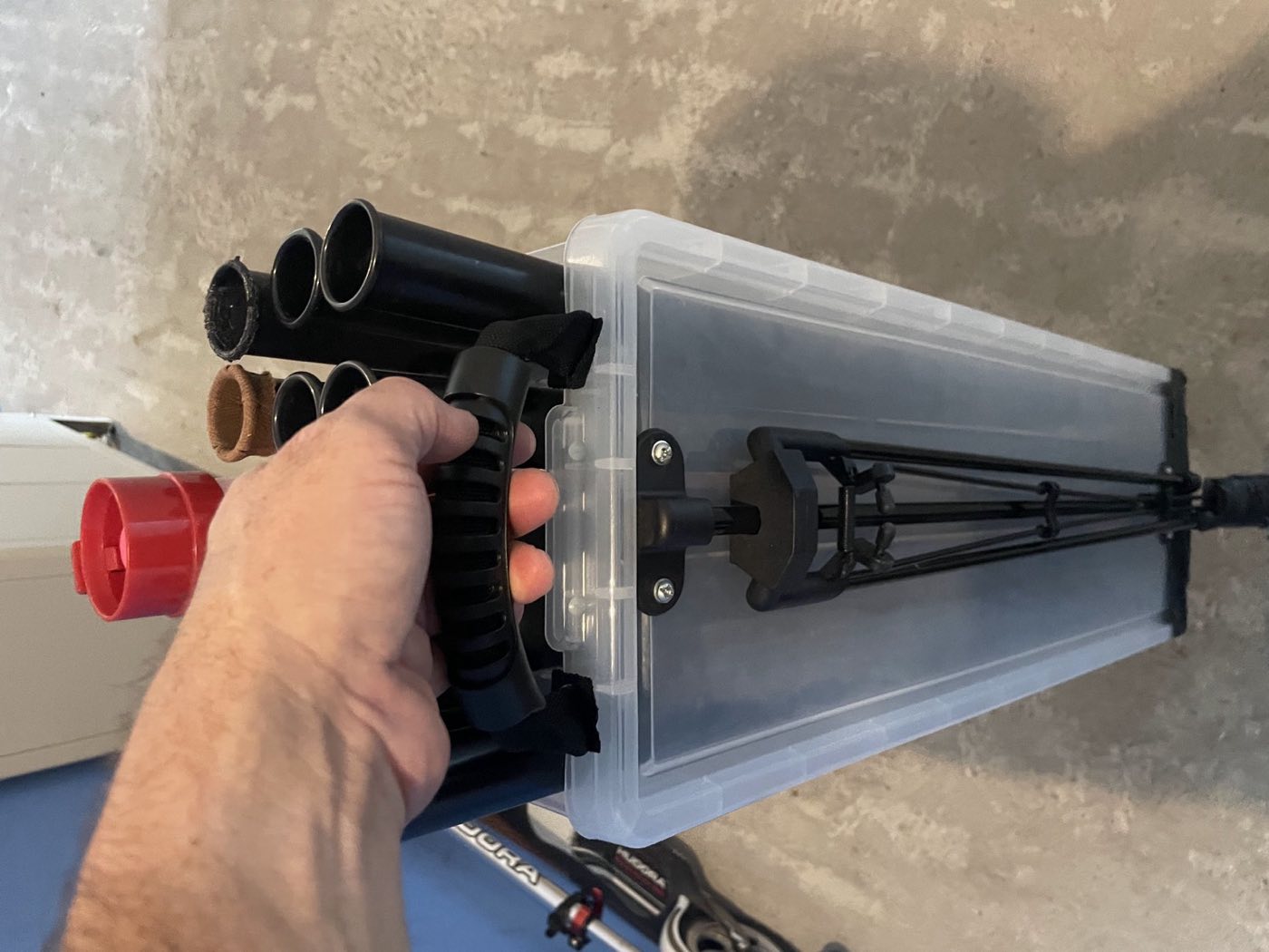 A hand lifting the prototype by its carry handle, with the stand leg folded flat underneath.