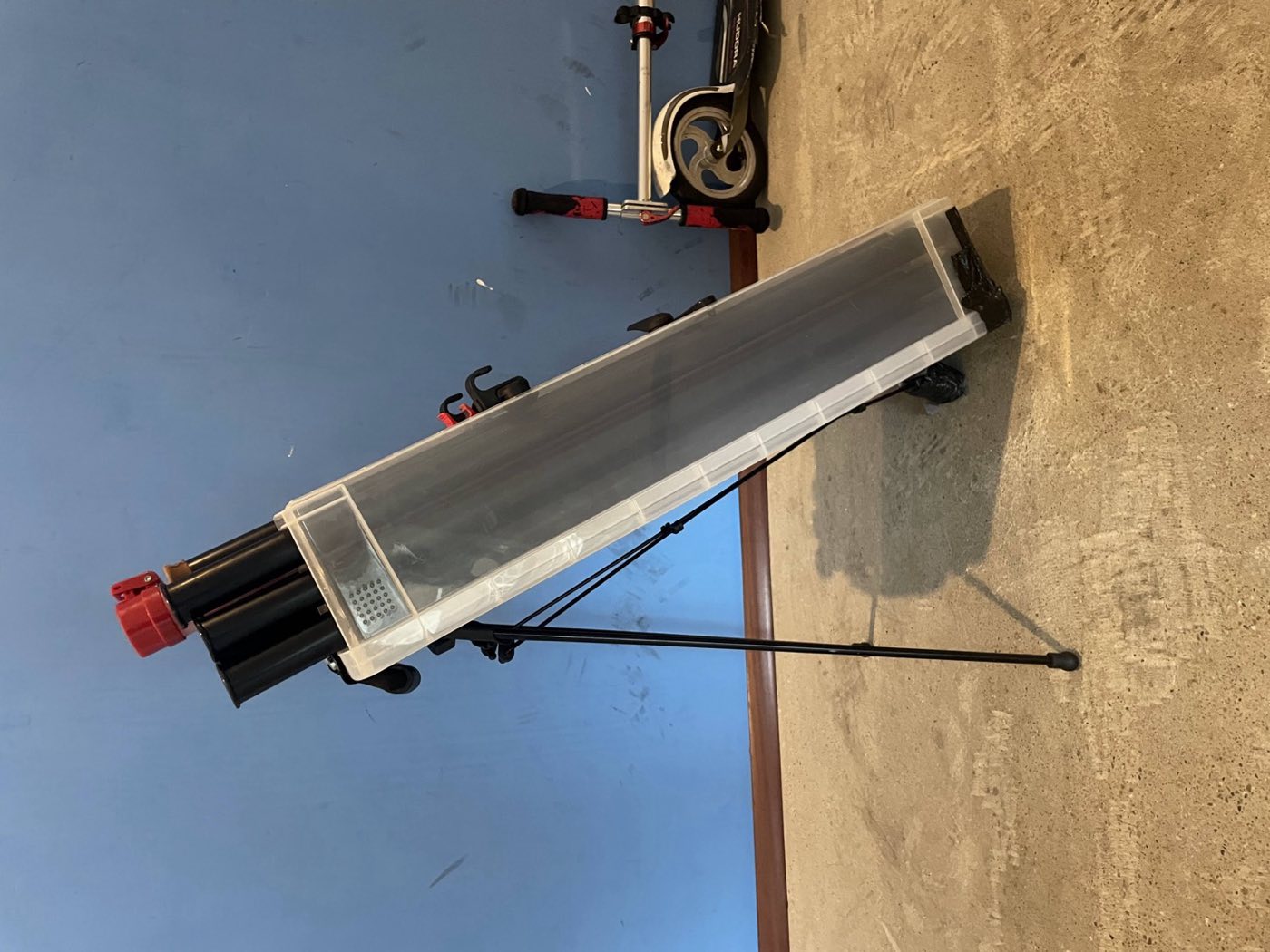 The VeloCaddie v3 prototype: a tall clear hard case holding golf clubs, standing upright on its fold-out leg.
